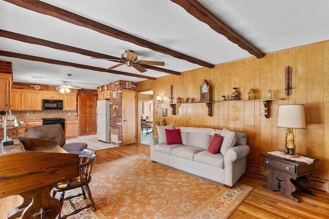 living area featuring ceiling fan, beamed ceiling, wooden walls, and light wood-style flooring