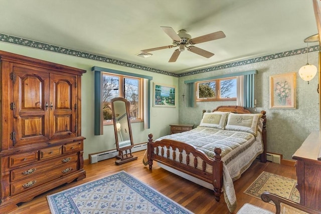 bedroom featuring multiple windows, a baseboard heating unit, and wood finished floors