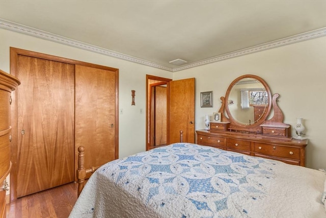 bedroom featuring a closet, visible vents, wood finished floors, and ornamental molding