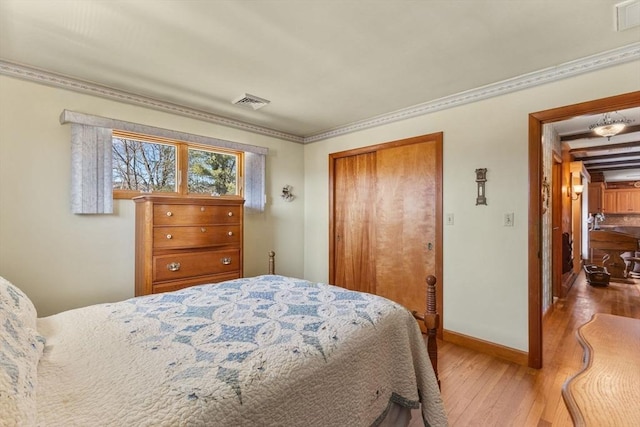 bedroom featuring visible vents, ornamental molding, hardwood / wood-style flooring, a closet, and baseboards