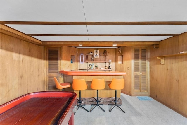 bar featuring tile patterned floors, beamed ceiling, wood walls, and a bar