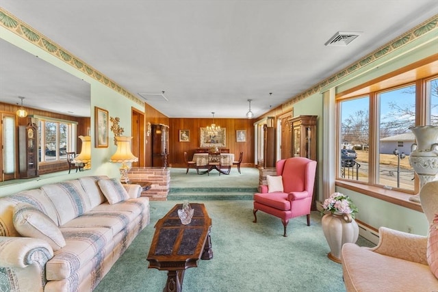 living area with visible vents, carpet, wooden walls, and a notable chandelier