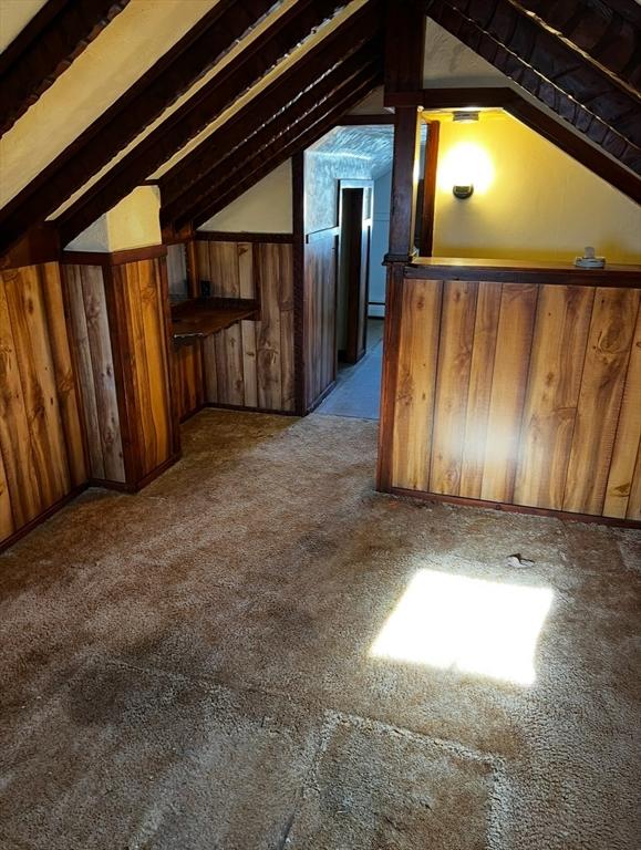 additional living space featuring carpet flooring, lofted ceiling, and wooden walls