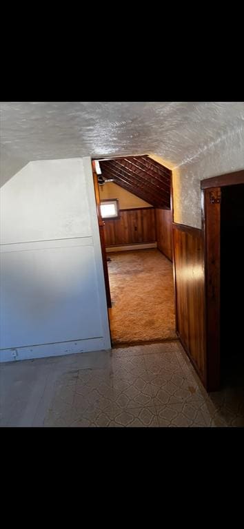 interior space featuring a textured ceiling, lofted ceiling, and wooden walls