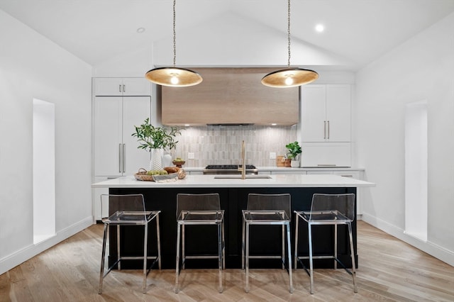 kitchen with white cabinets, decorative light fixtures, light wood-type flooring, and a kitchen island with sink