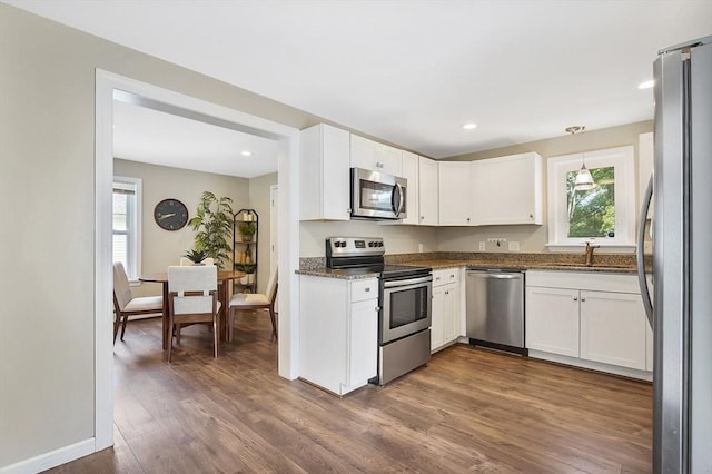 kitchen featuring stainless steel appliances, a sink, white cabinets, dark stone counters, and pendant lighting