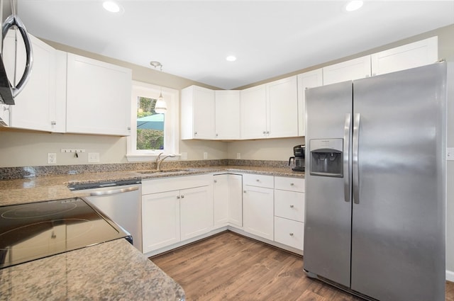 kitchen with sink, appliances with stainless steel finishes, wood-type flooring, light stone counters, and white cabinetry