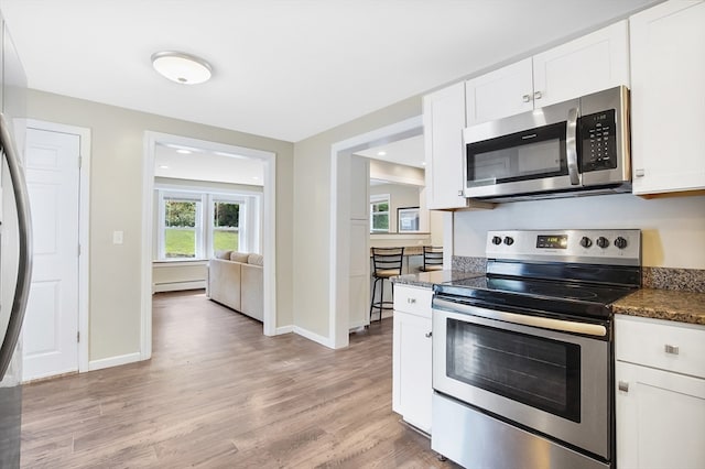 kitchen featuring dark stone counters, light hardwood / wood-style flooring, white cabinetry, a baseboard heating unit, and stainless steel appliances