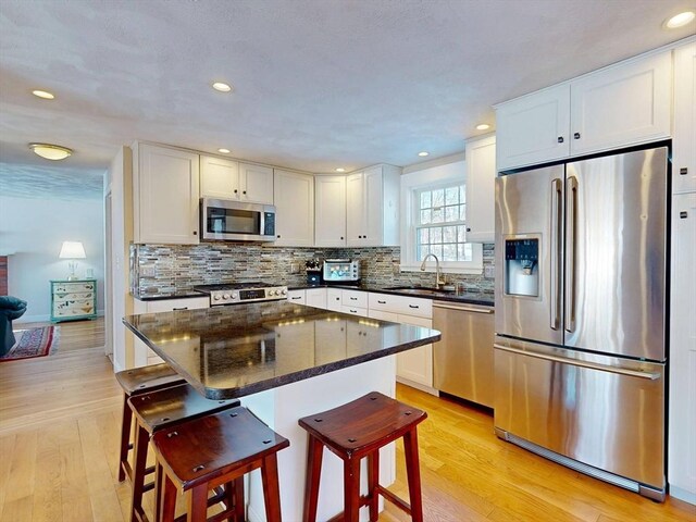 kitchen featuring light wood finished floors, appliances with stainless steel finishes, a breakfast bar area, and white cabinets