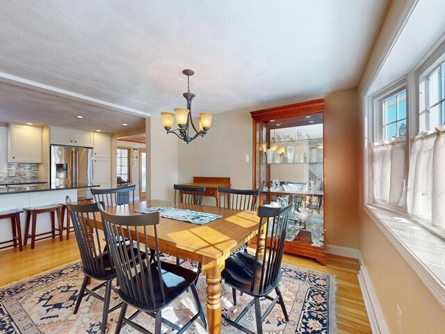 dining area with baseboards, recessed lighting, light wood-type flooring, and an inviting chandelier