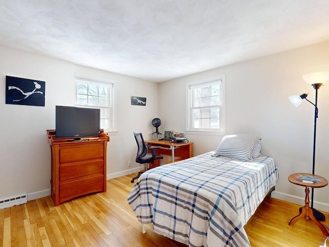 bedroom featuring a baseboard heating unit, baseboards, multiple windows, and light wood finished floors