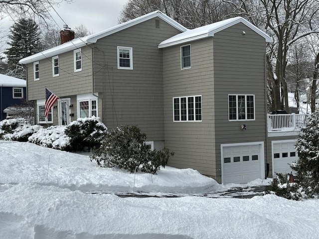 snow covered property with a chimney and an attached garage