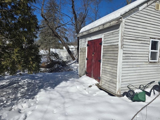 snow covered structure featuring an outbuilding and a storage unit