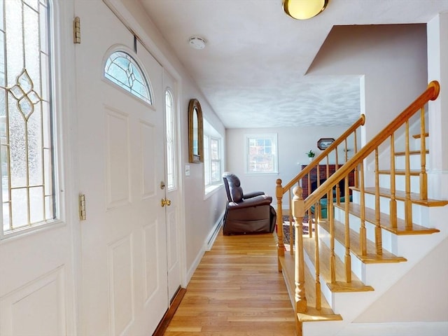 entryway featuring baseboards, light wood finished floors, and stairs