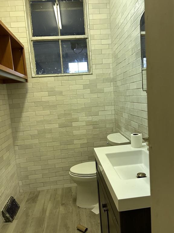 half bathroom featuring toilet, vanity, wood finished floors, and tile walls