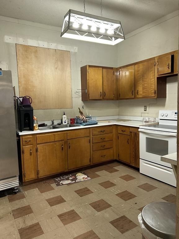 kitchen featuring white electric range oven, freestanding refrigerator, a sink, light countertops, and light flooring