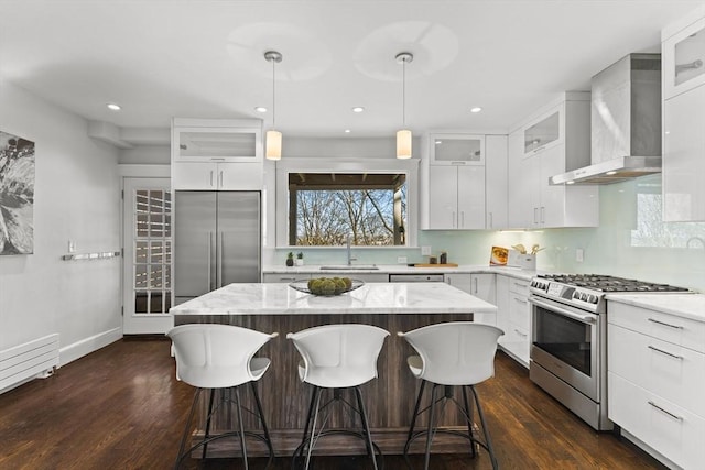 kitchen with a kitchen island, a breakfast bar, appliances with stainless steel finishes, wall chimney exhaust hood, and a sink