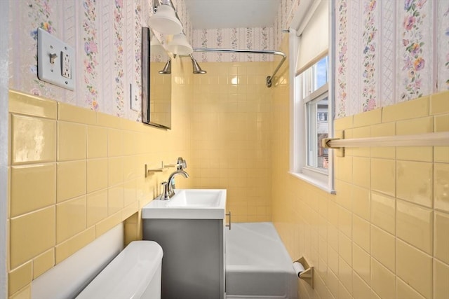 full bathroom featuring tiled shower / bath combo, toilet, and tile walls