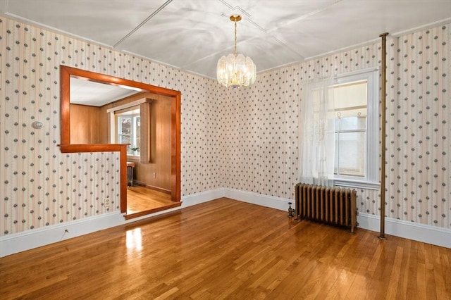 spare room with wood-type flooring, radiator heating unit, ornamental molding, and a notable chandelier