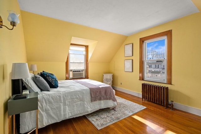 bedroom with wood-type flooring, multiple windows, radiator, and vaulted ceiling