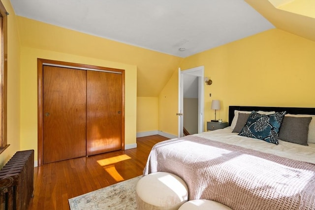 bedroom with a closet, vaulted ceiling, radiator, and hardwood / wood-style floors