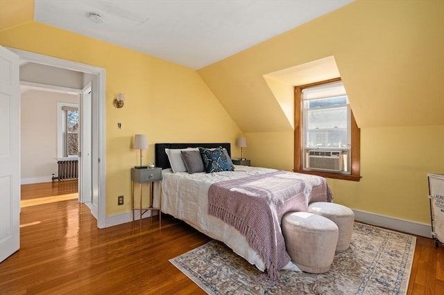 bedroom with radiator heating unit, multiple windows, vaulted ceiling, and hardwood / wood-style floors