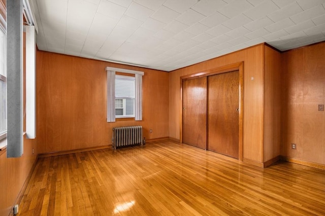 unfurnished bedroom with wood walls, radiator heating unit, a closet, and light wood-type flooring