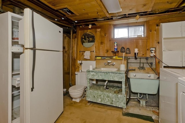 basement with white refrigerator, wooden walls, separate washer and dryer, and sink