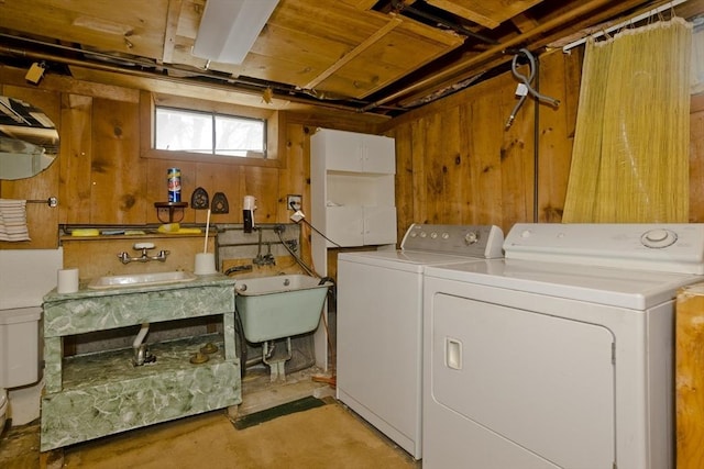 clothes washing area with sink, wooden walls, and washer and dryer