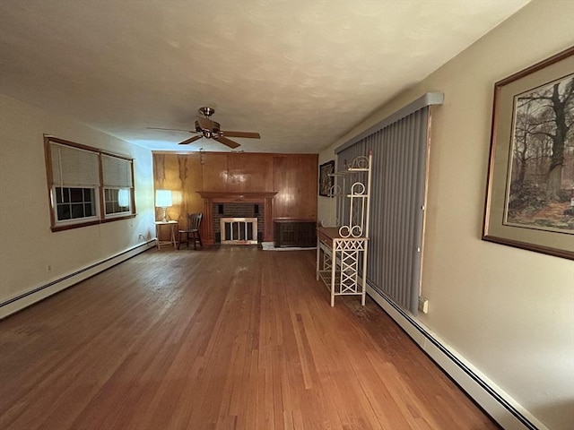 unfurnished living room with a brick fireplace, a baseboard radiator, wood-type flooring, and ceiling fan