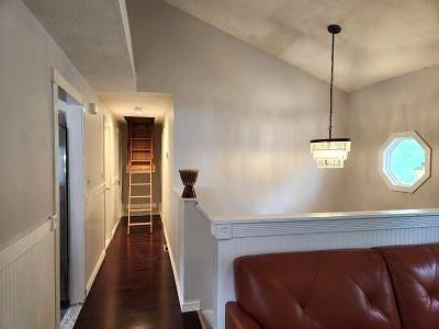 corridor featuring dark wood finished floors, baseboards, and a chandelier