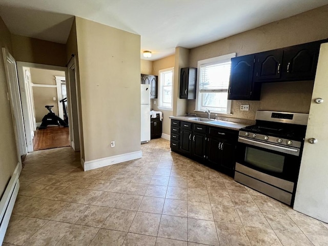 kitchen with sink, stainless steel gas range oven, a baseboard heating unit, white refrigerator, and light tile patterned floors