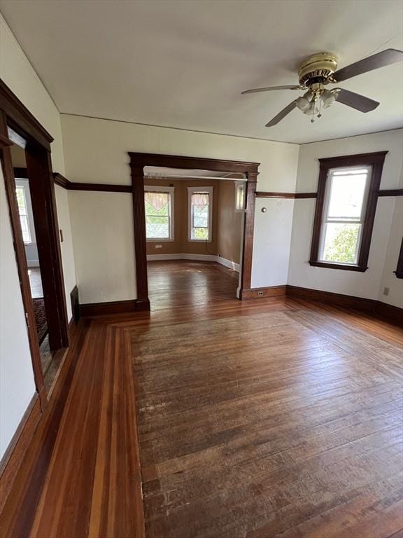 empty room with ceiling fan, a healthy amount of sunlight, and dark hardwood / wood-style floors