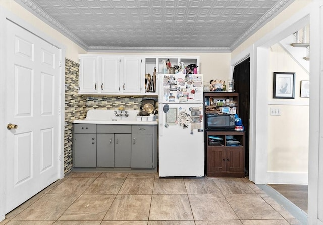 kitchen with gray cabinetry, backsplash, ornamental molding, and white refrigerator