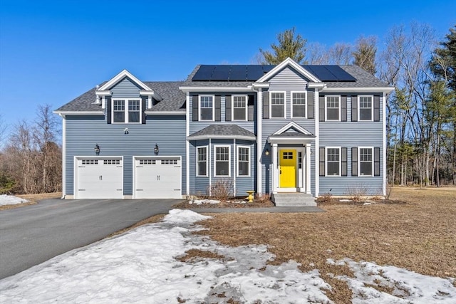 colonial house featuring solar panels, aphalt driveway, and roof with shingles