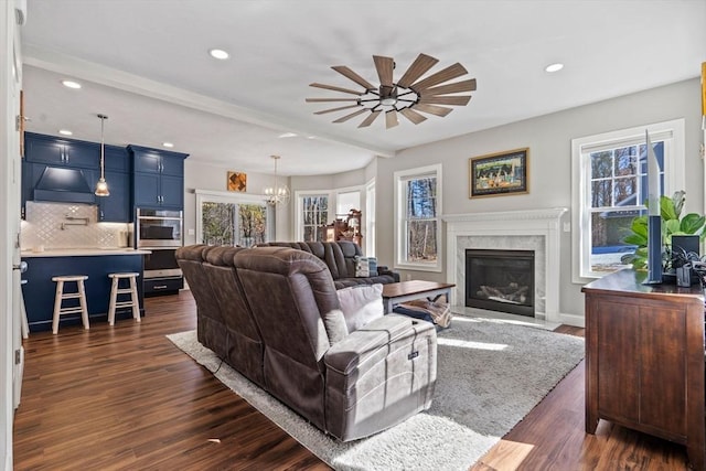 living area with ceiling fan with notable chandelier, dark wood-type flooring, a fireplace, and recessed lighting