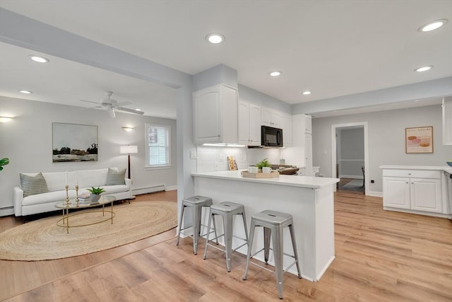 100 Summit, Brookline, MA 02446 - kitchen with black microwave, a baseboard heating unit, white cabinets, a breakfast bar, and recessed lighting