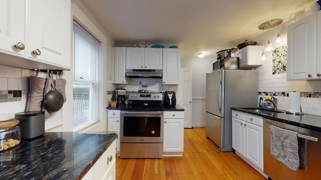 kitchen with white cabinets, light wood-style floors, stainless steel appliances, under cabinet range hood, and a sink