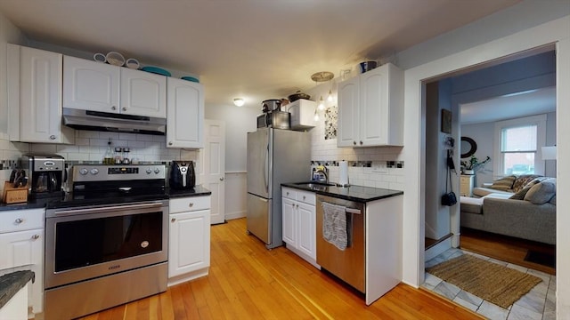 kitchen with stainless steel appliances, dark countertops, white cabinets, and under cabinet range hood