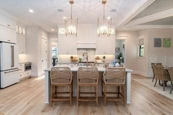 kitchen featuring a kitchen island with sink, white cabinets, a kitchen breakfast bar, white refrigerator, and decorative light fixtures