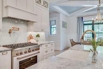 kitchen featuring white cabinetry, light stone counters, high end stove, and a healthy amount of sunlight