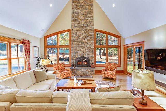 living room with a stone fireplace, high vaulted ceiling, and light hardwood / wood-style flooring