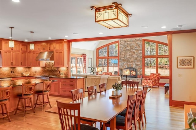 dining room featuring vaulted ceiling, a stone fireplace, crown molding, and light hardwood / wood-style flooring