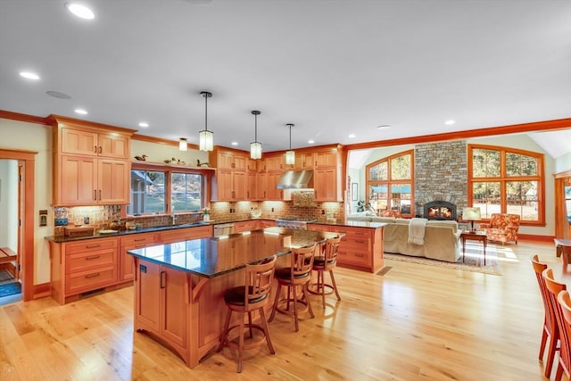 kitchen with dark stone countertops, decorative light fixtures, a center island, and light wood-type flooring