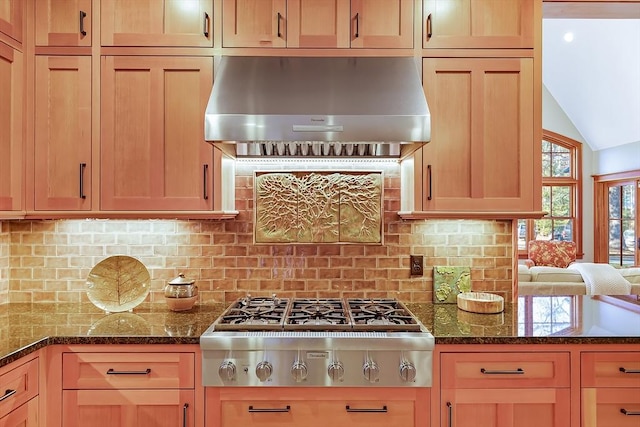 kitchen featuring lofted ceiling, dark stone countertops, decorative backsplash, stainless steel gas cooktop, and wall chimney exhaust hood