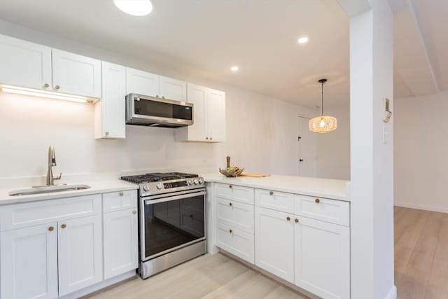 kitchen with light wood-type flooring, a sink, appliances with stainless steel finishes, white cabinets, and light countertops