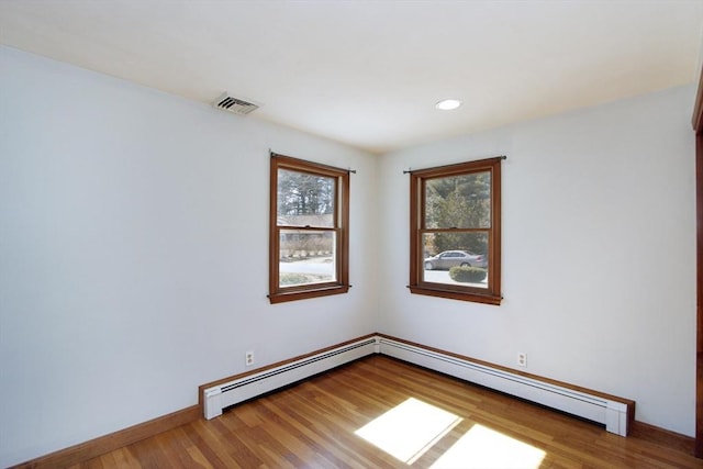 spare room featuring visible vents, baseboards, wood finished floors, and a baseboard heating unit