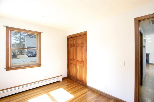 unfurnished bedroom featuring a closet, baseboard heating, light wood-type flooring, and baseboards