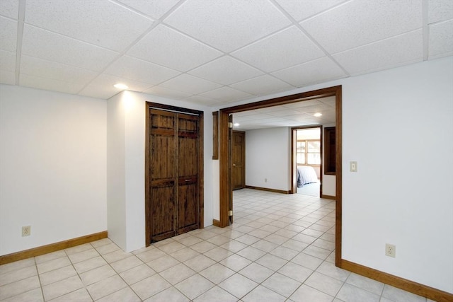 empty room featuring light tile patterned floors, a drop ceiling, and baseboards