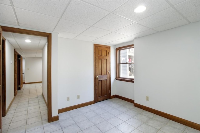 spare room with light tile patterned flooring, a paneled ceiling, and baseboards